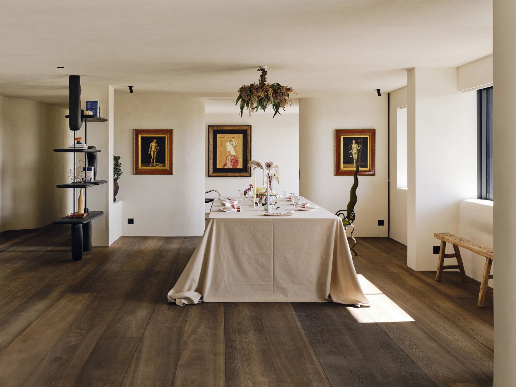 A dining table in a sunlit room with timber floors and carefully placed artwork