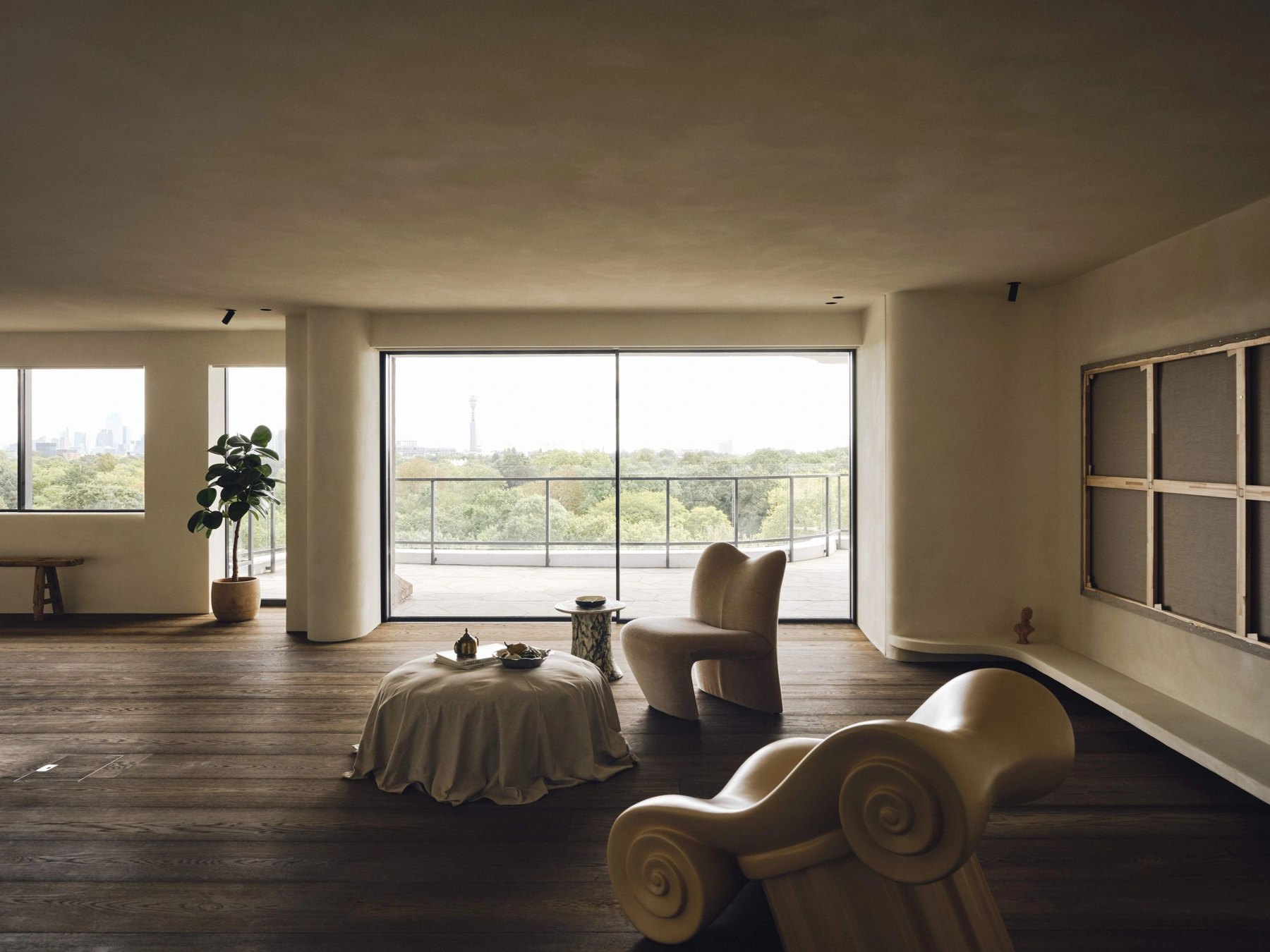 A sunlit living room with sculptural seating, timber flooring and broad views across the landscape