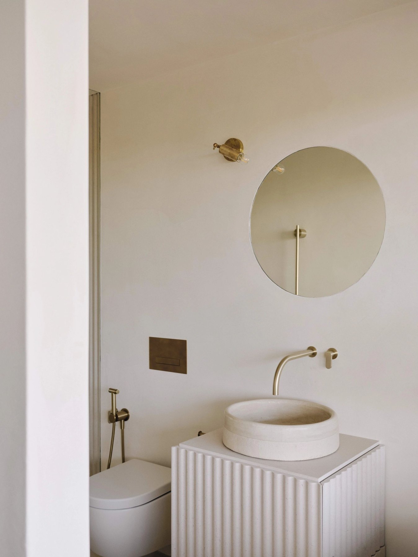 A circular mirror above a sculptural basin with brass fittings